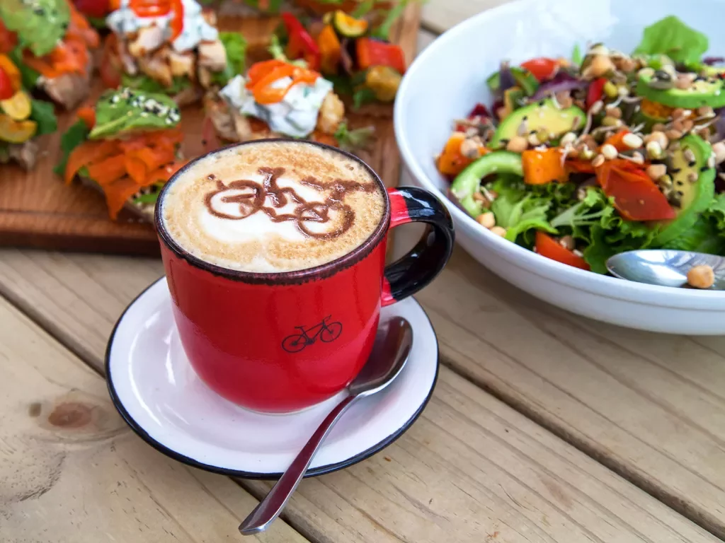 Table with platters of food and a cappuccino with a bicycle drawn in the foam