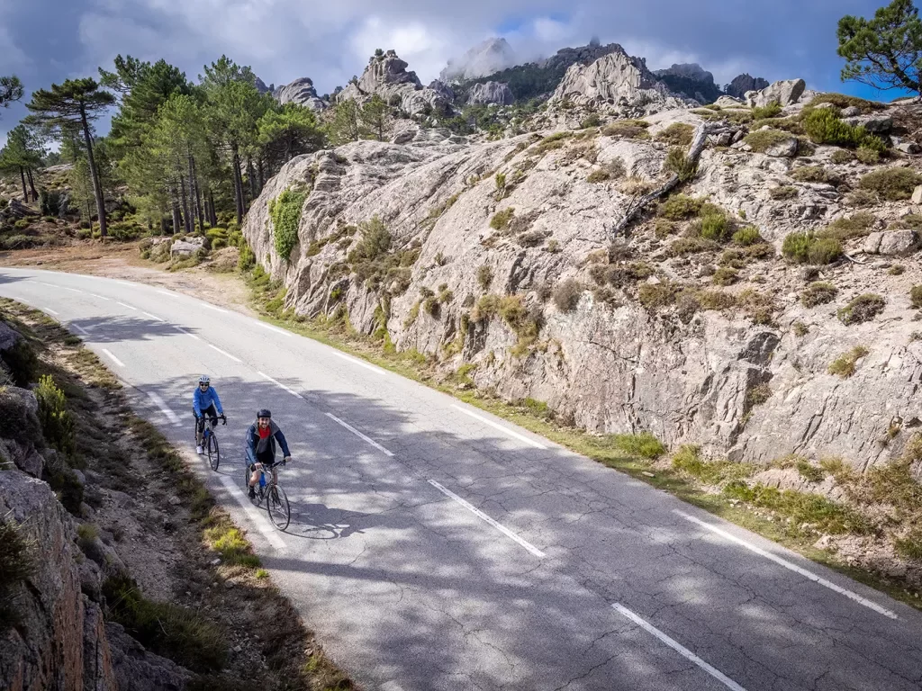 Two guests cycling down road, between large, craggy rock faces.