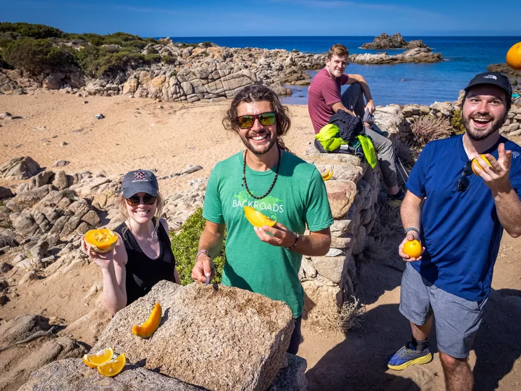 Four guests/leaders on a rocky beach, all eating fruit, one is juggling oranges.