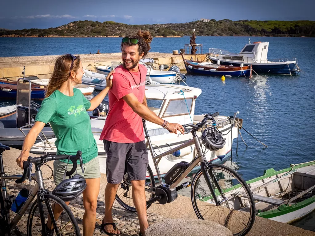 Two guests with bikes, walking along pier, boats around them.