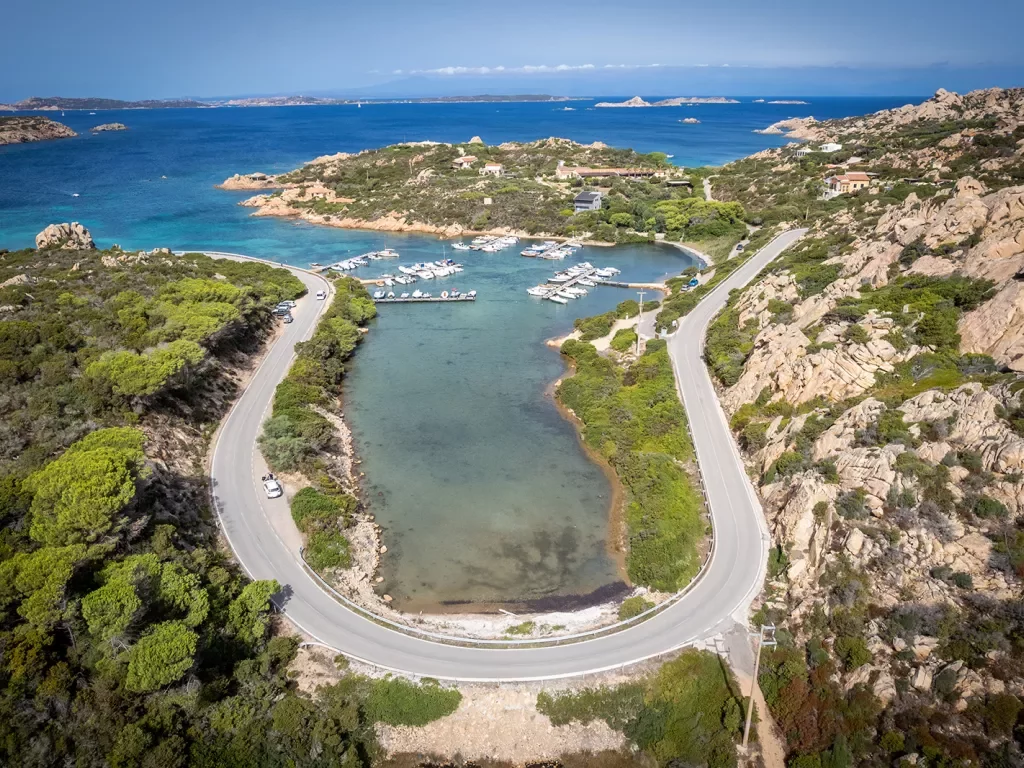 Bird's eye shot of a "U" shaped road on the Italian coastline, small boats and piers in distance.