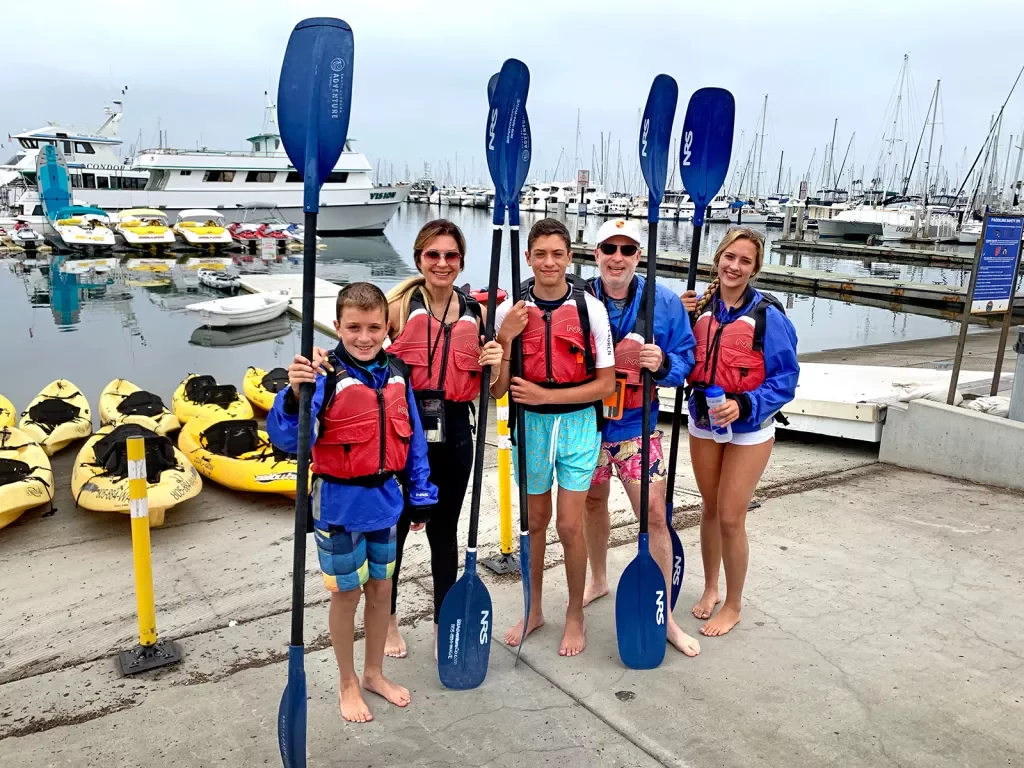 Five guests getting ready to kayak, oars in hand.