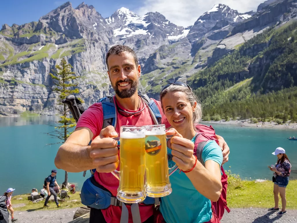 Two guests w/ beer in front of lake, mountains in background.