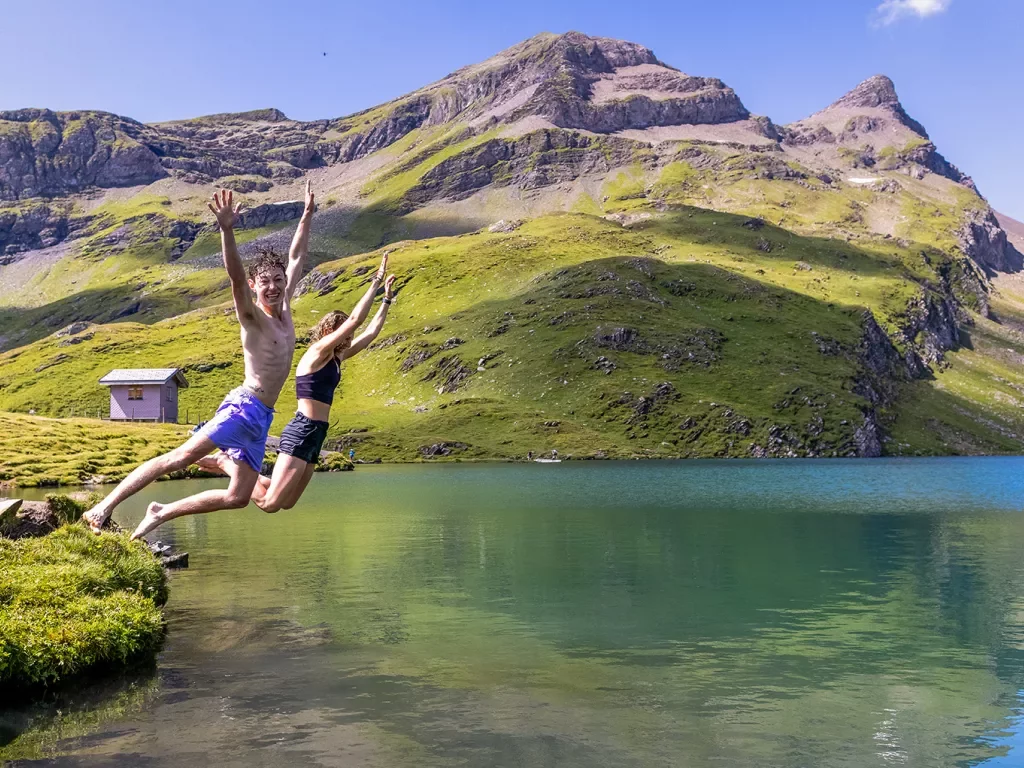 Two guests jumping into small lake, sharp cliffs and small shack in background.