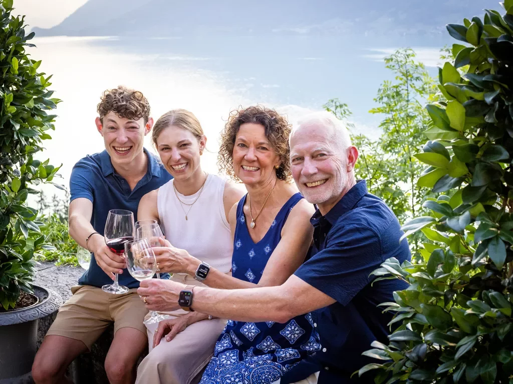 Four guests cheersing wine glasses, large lake or ocean behind them.