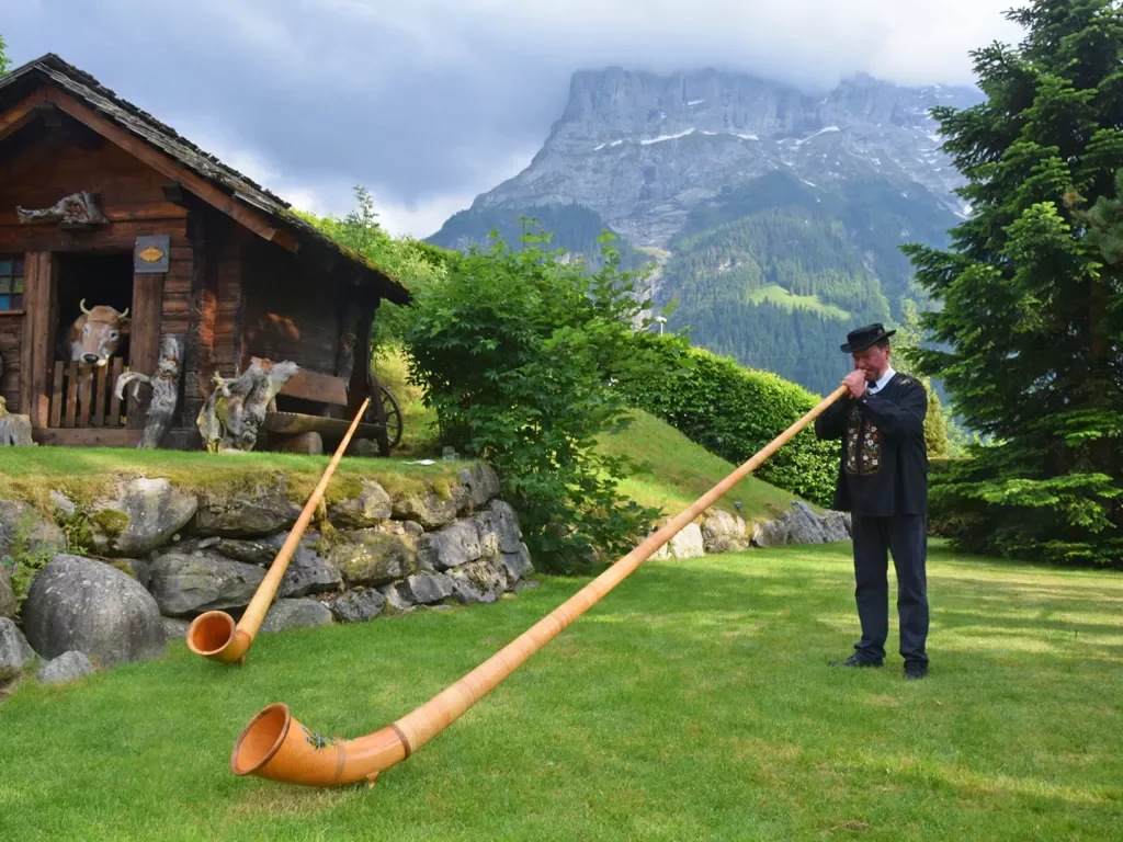 Local man playing a Swiss Horn, wooden shack in background.