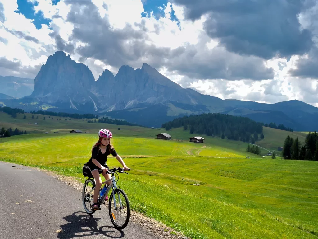 Young guest cycling down mountain road, large range and meadow in background.