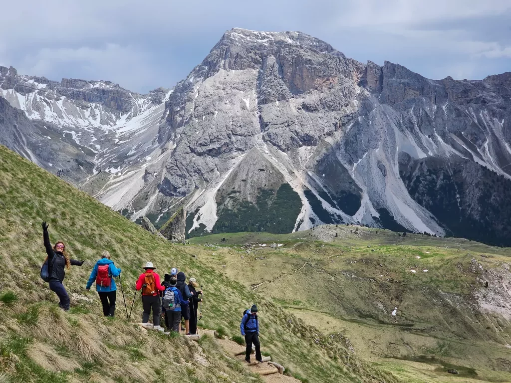 Group of guests hiking down mountain trail. Dolomites in background.