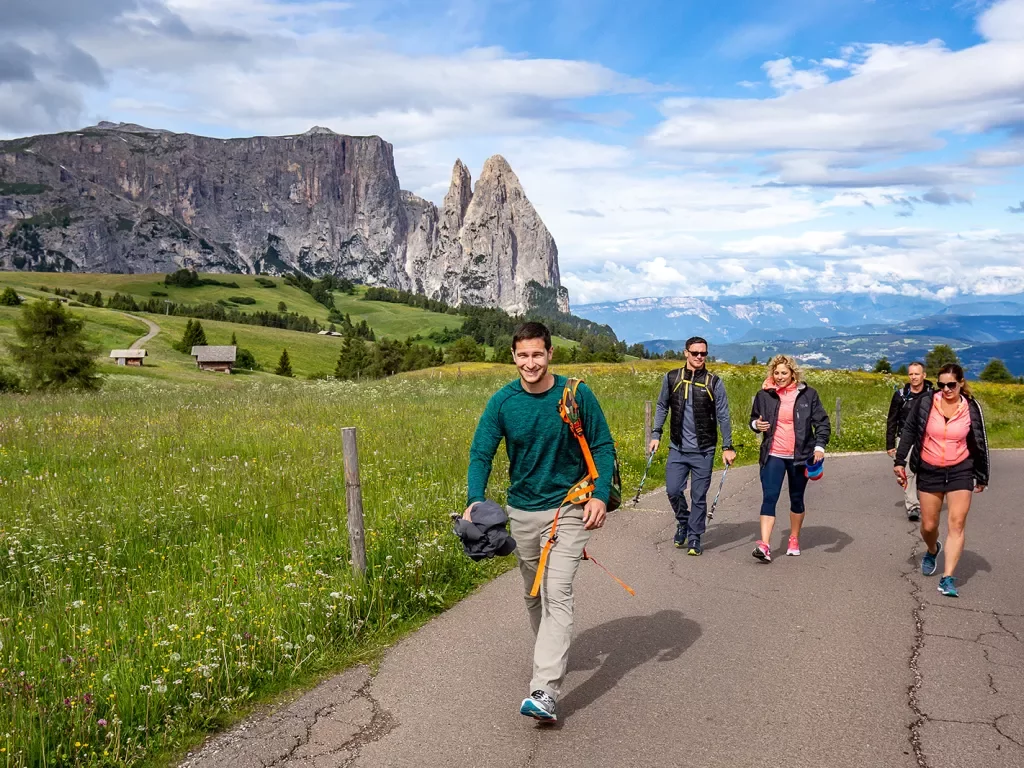 Five guests walking up hillside road, large cliffs, small houses in distance.