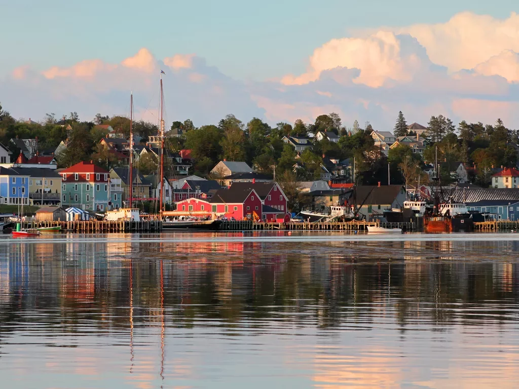 Wide shot of seaside town at sunset, vibrant red houses scattered throughout.