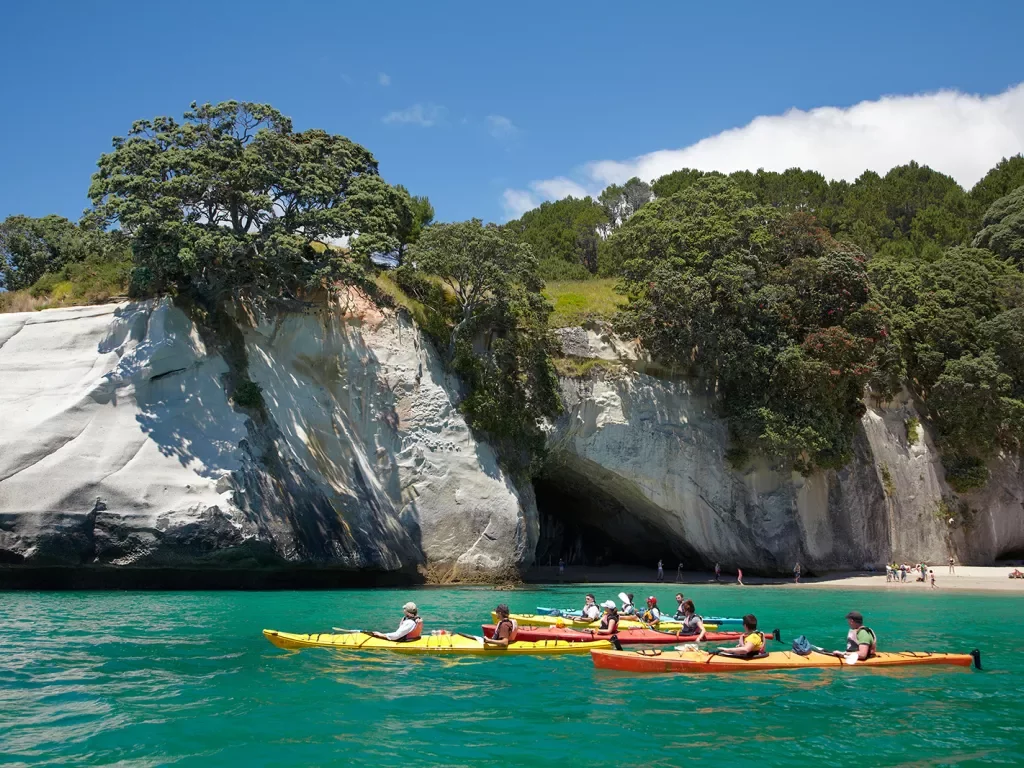 Guests kayaking away from beach, white stone cliff behind them. 