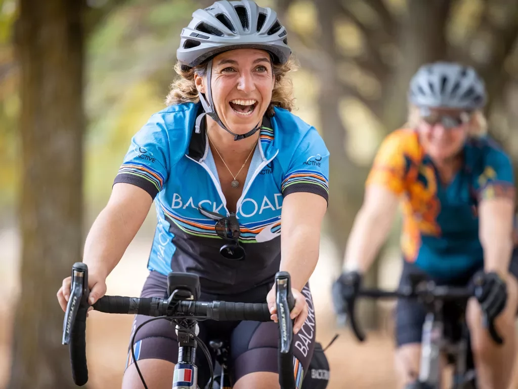 Close-up of two guest in cycling gear on bikes, one laughing.