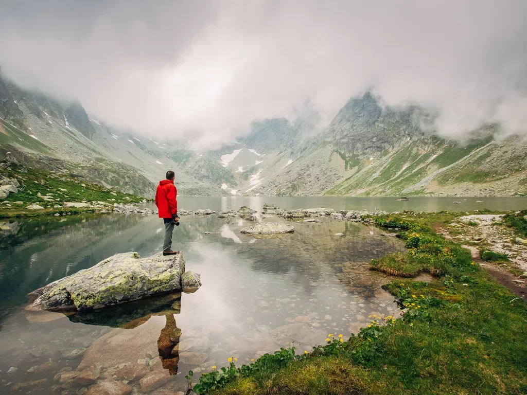 Man in red coat standing in middle of misty lake.