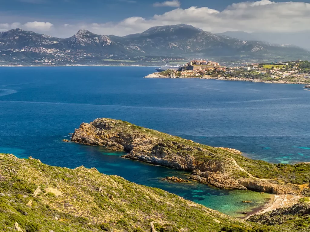 Wide shot of Italian lakeside, large peninsula, hills, coastal town in distance.