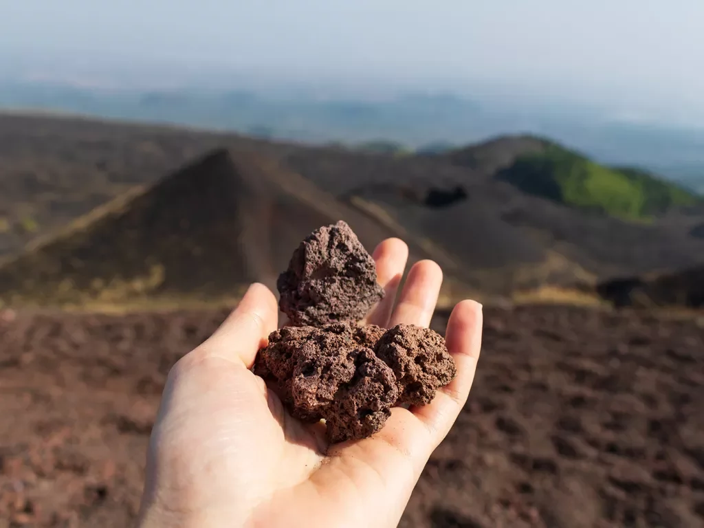 Point of view shot of volcanic rock landscape, hand holding volcanic rocks.