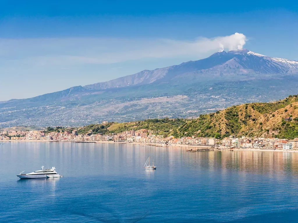 Wide shot of Mount Etna, small boats in water in foreground.