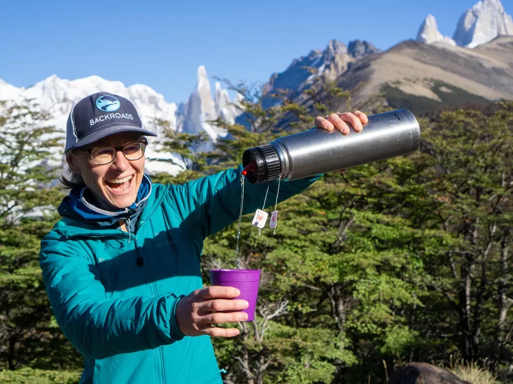Leader pouring water into yerba mate infuser, trees, snowy peaks behind them.