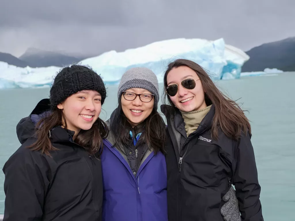 Three young guests smiling, large lake and glacier behind them.