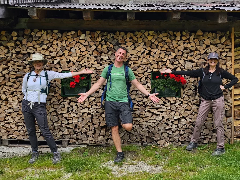 Three guests in front of wooden building, one in center, the other two gesturing to them.