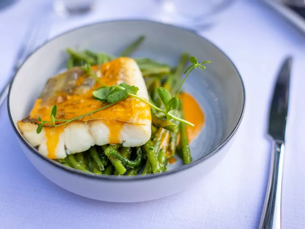 Plate of pan fried fish with an orange sauce, bed of greens.