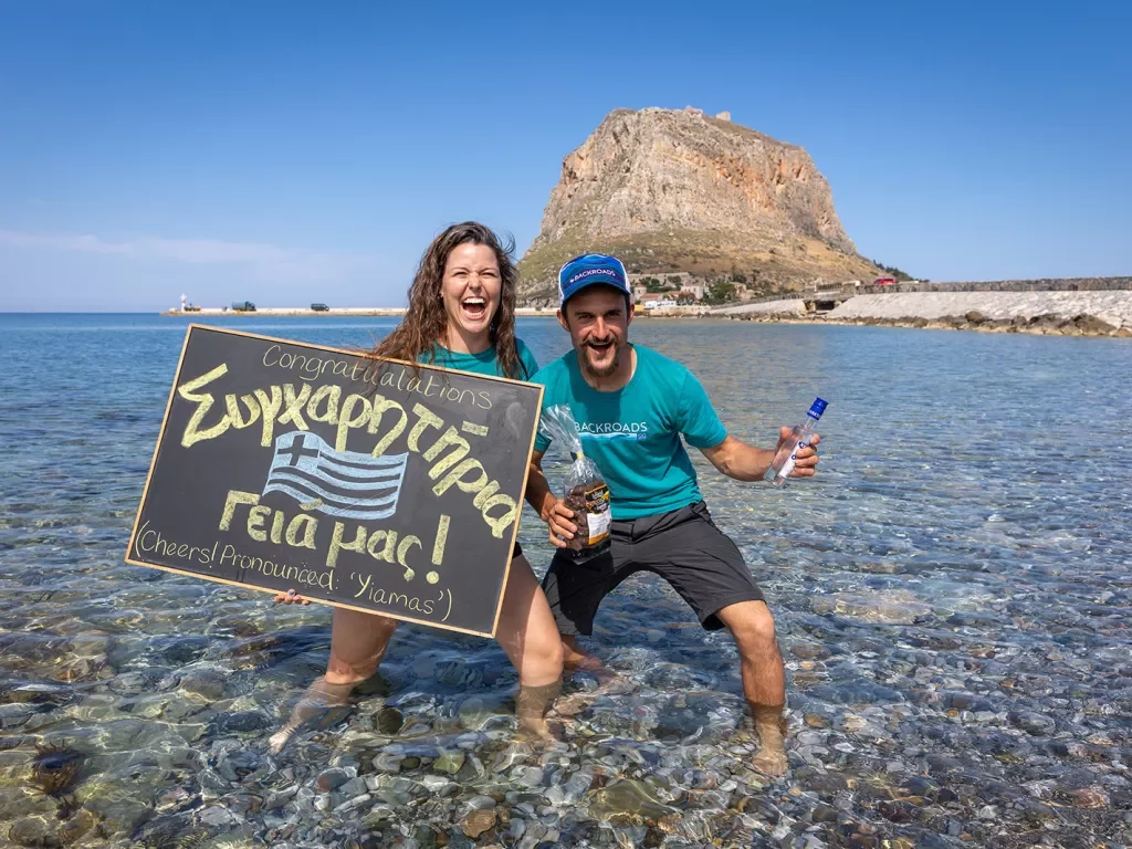 Two leaders holding Greek lettered "Congratulations" signage, standing in shallow water.