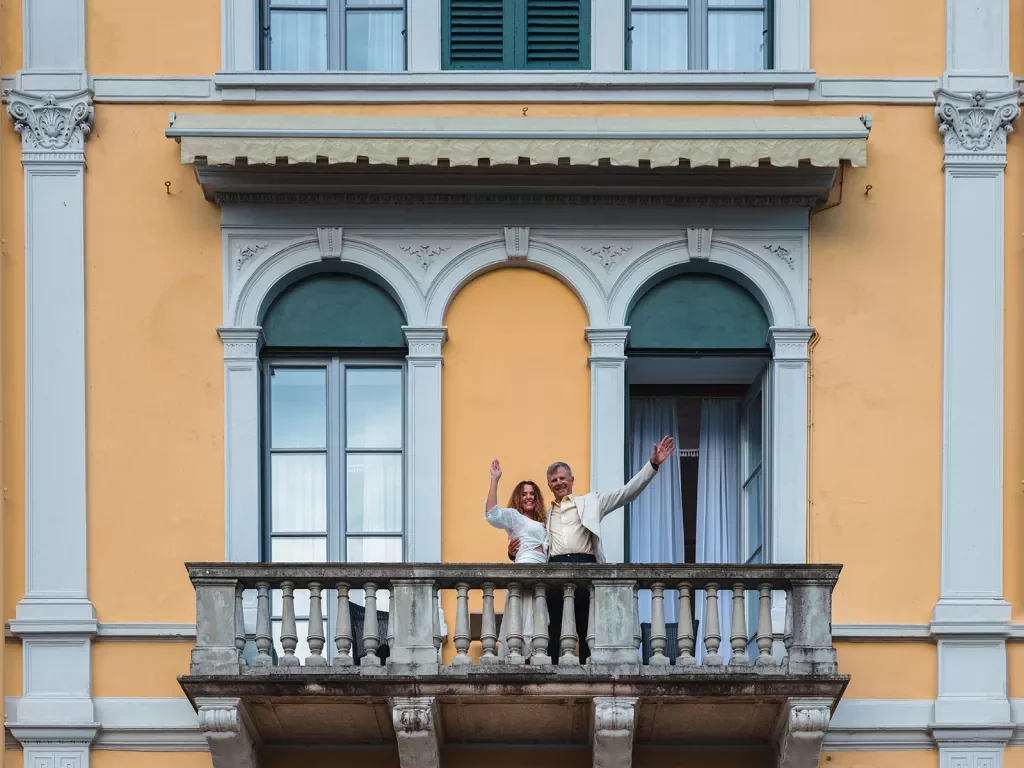 Two guests on balcony, waving to camera. 