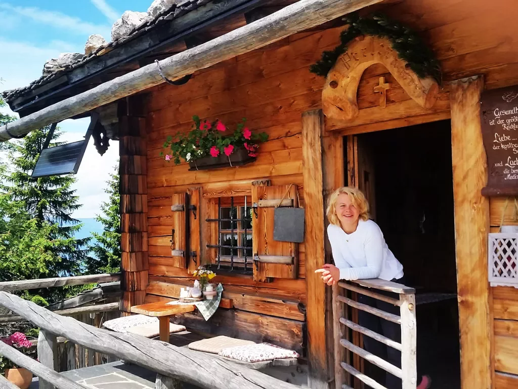 Woman leaning on balcony off of log cabin.