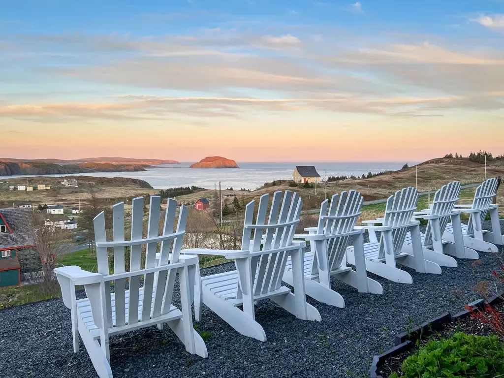 Wide shot of grassy ocean vista, white chairs in foreground.