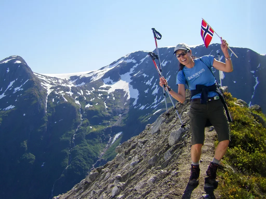 Woman celebrating reaching the summit holding miniature flag of Norway.