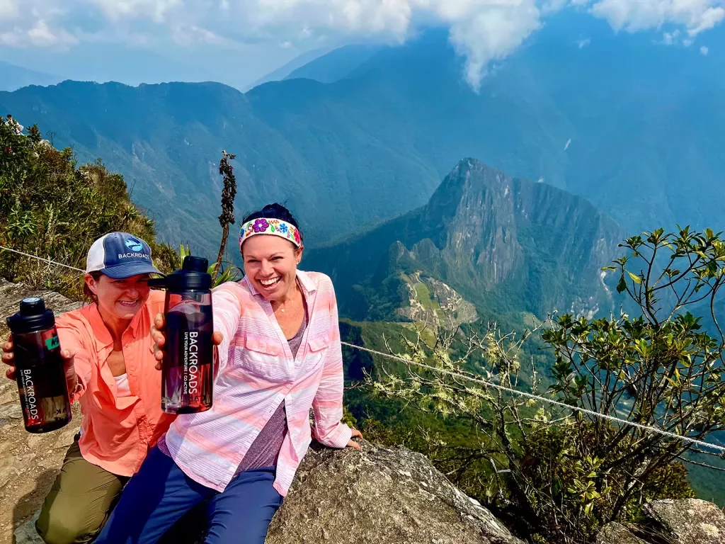 Two guests on mountaintop, showing camera BR water bottles.