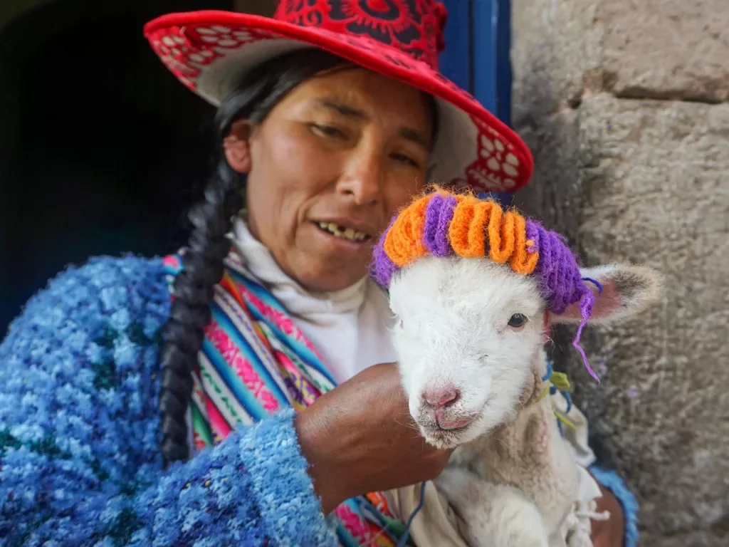 Local woman holding a small white goat, both facing camera.