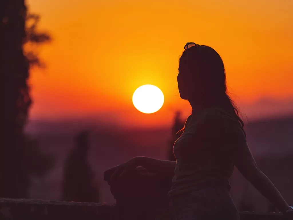 Woman backlit in front of vibrant sunset horizon.