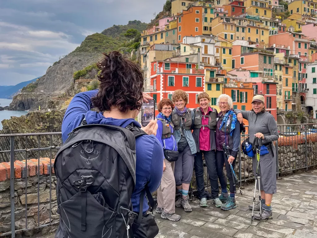 Over the shoulder shot of guest taking photo of other guests. Colorful Italian houses and coast in background.