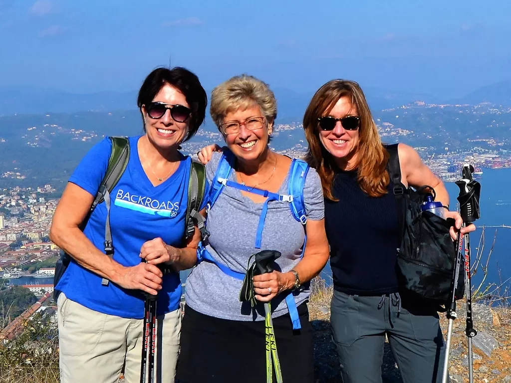 Three women posing together with Italian landscape behind them.