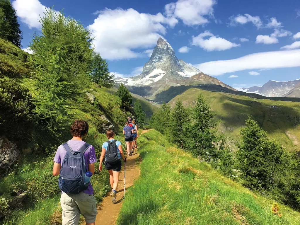Group of guests on hillside trail, Matterhorn in distance.