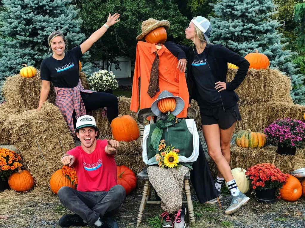 Three guests posing with pumpkin-headed scarecrows.