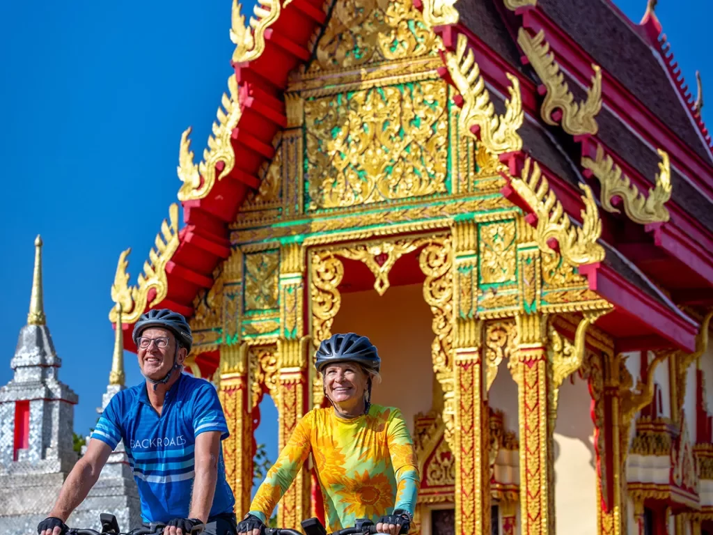 Two people biking in front of a colorful temple