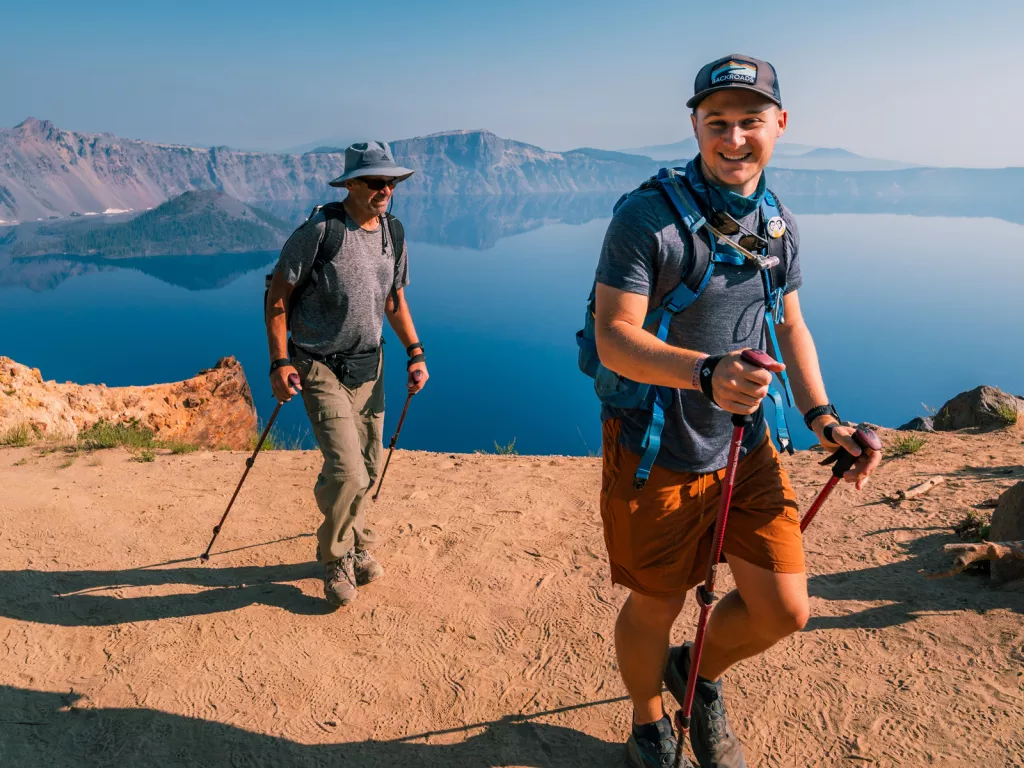 Two men ascending a dirt trail, while using hiking poles
