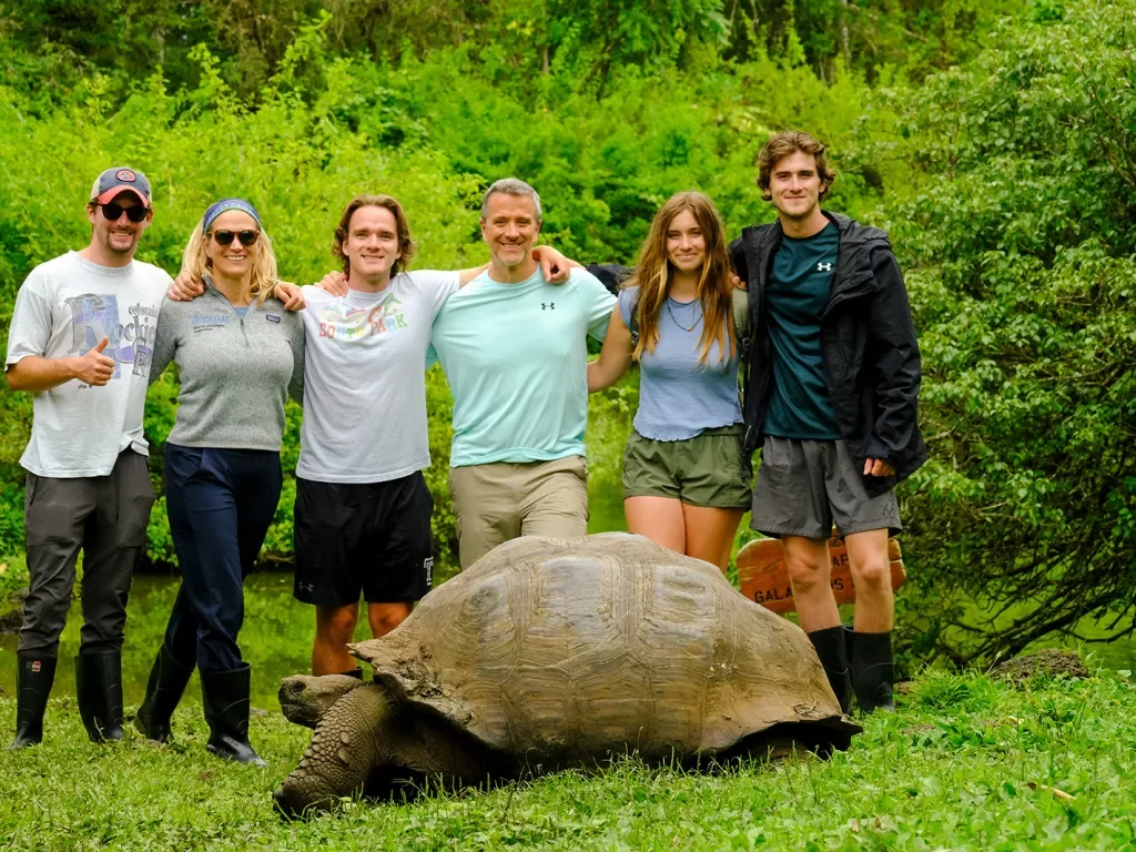 Tourists pose behind a tortoise