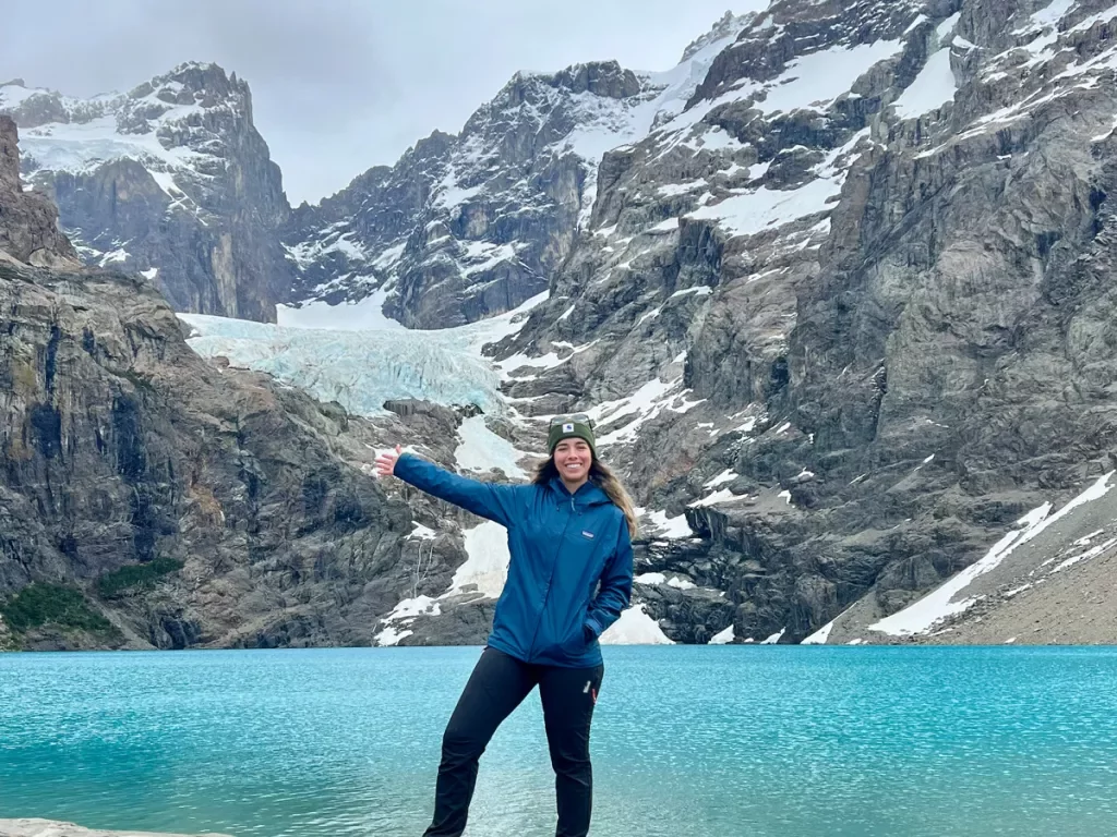 A person giving a thumbs up in front of a blue lake