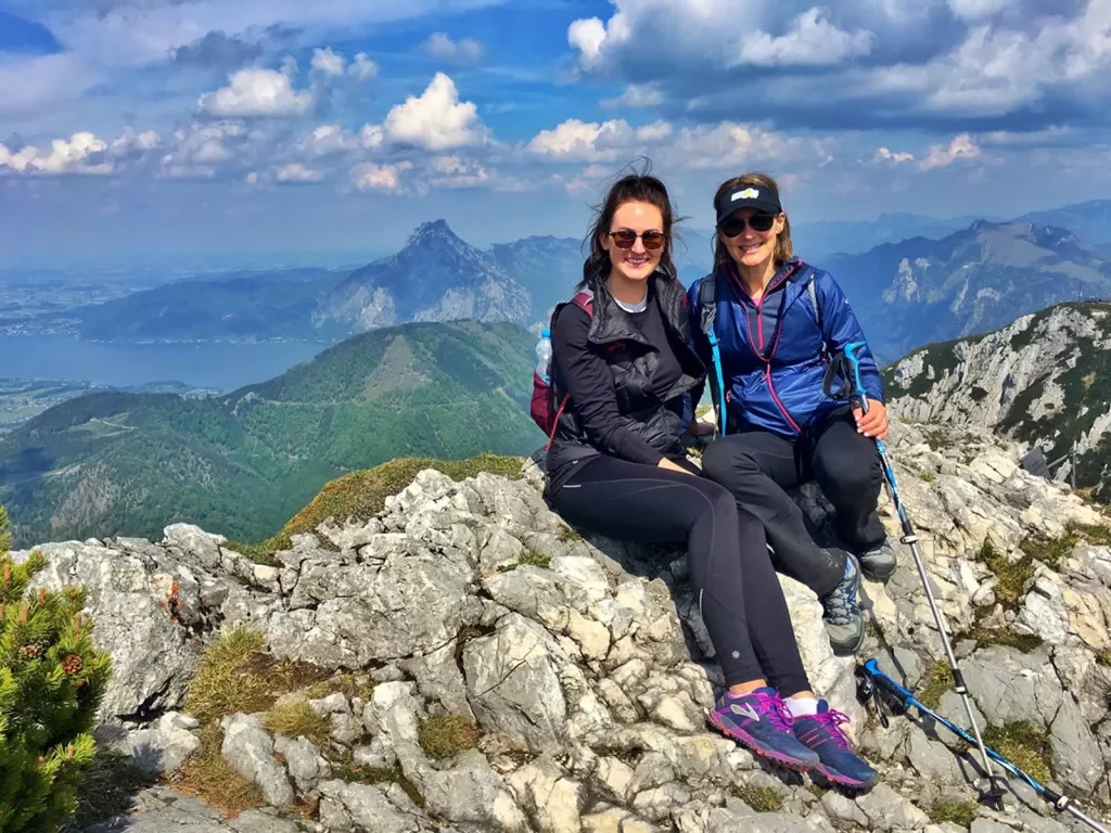 Two women sitting on a pile of rocks at the top of a mountain