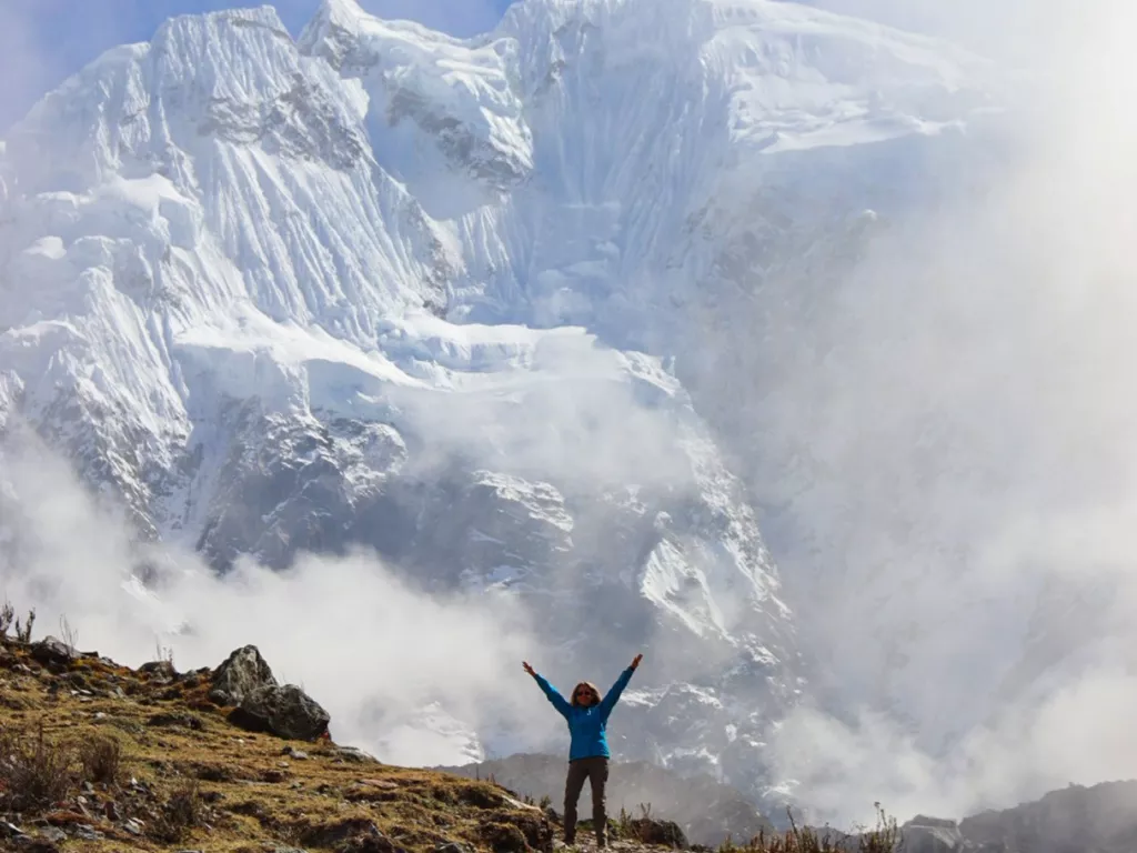 Person standing on top of a cliff with cloudy skies behind