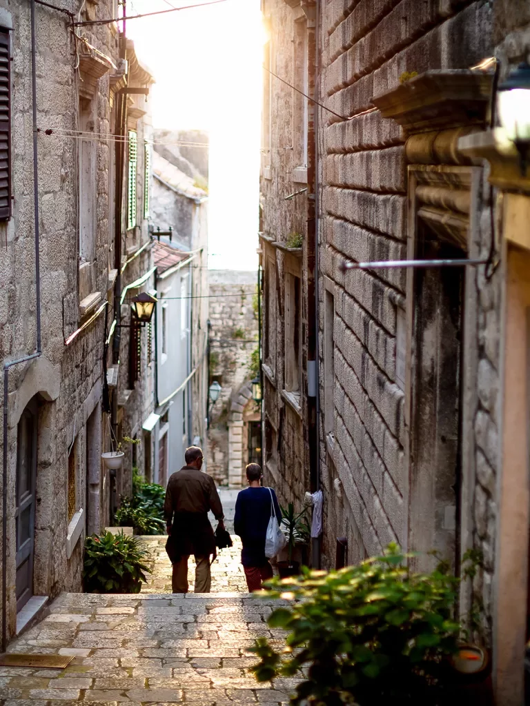 Two people walking down narrow alleyway during sunset.
