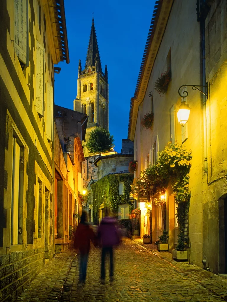 Two guests walking down French alleyway, church spire in front of them.