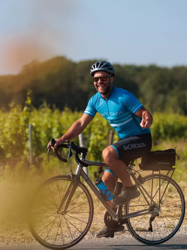 Guest cycling past grapevines, showing peace sign to camera.