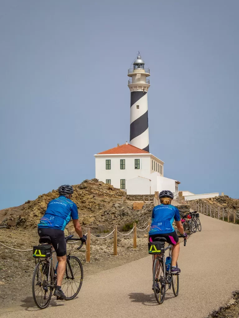 Bikers riding towards a lighthouse.