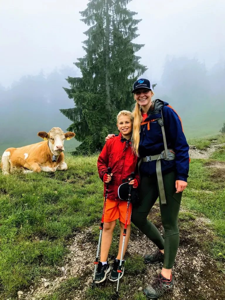 Hiker posing with child and cow on a misty trail.