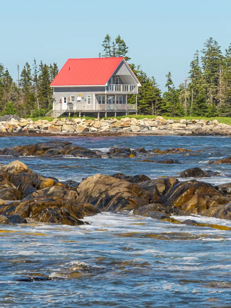Rocky ocean shore in foreground, two-story fishing house in background.