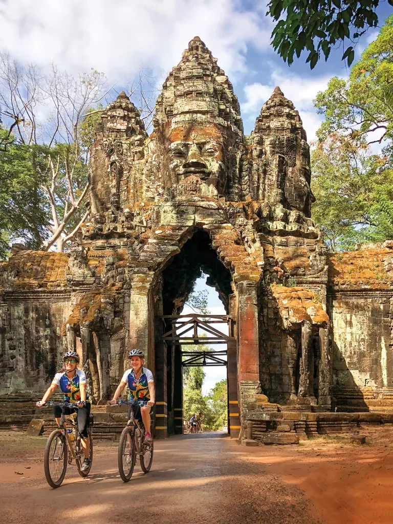 Two guests biking through Angkor Wat sculpture archway.
