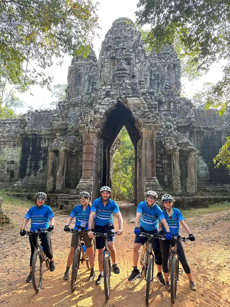 Group of Backroads guests posing in front of Angkor Wat on their bikes